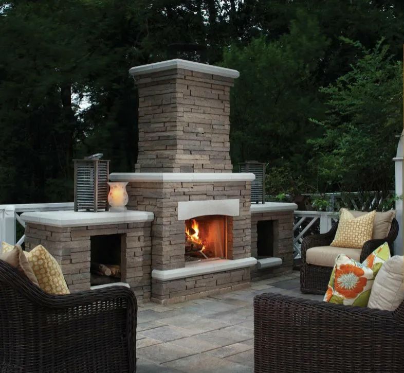 Outdoor stone fireplace with seating on a patio, fire burning.