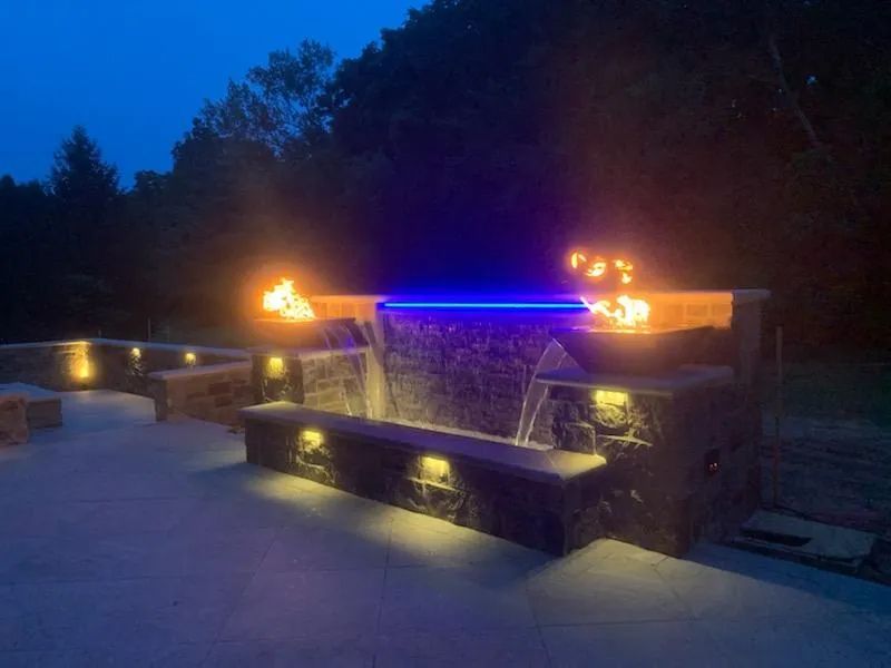 Water feature with cascading falls, fire pits, and blue LED lights at dusk.