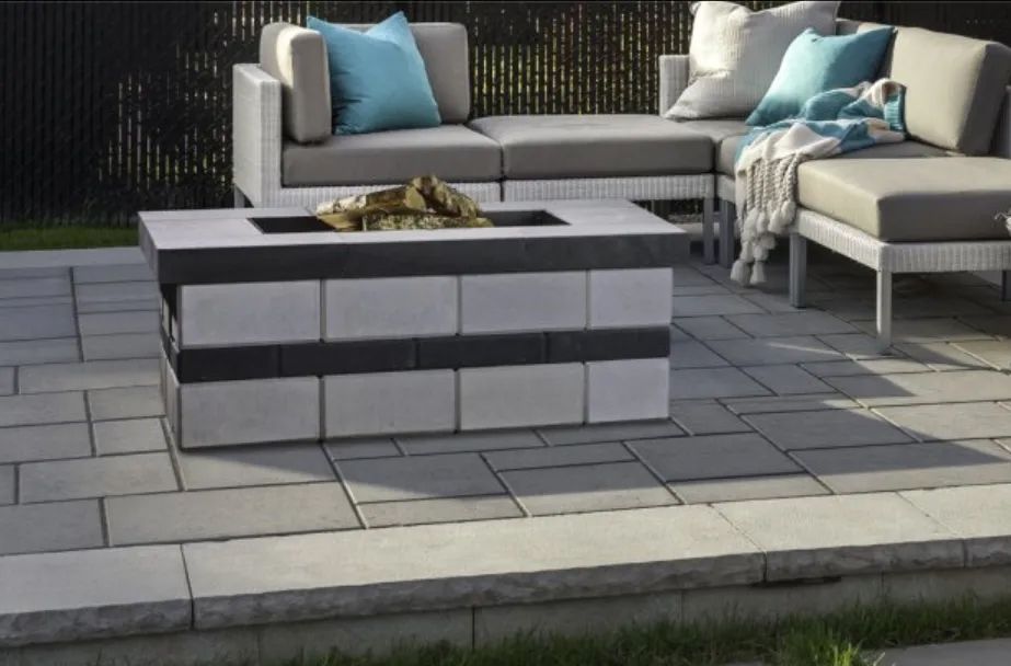 Patio with a fire pit made of stone blocks, and gray outdoor seating with blue pillows.