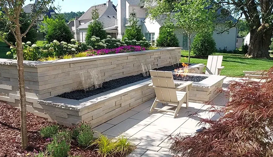 Backyard patio with fire pit, seating, and stacked stone wall with landscaping and water feature.