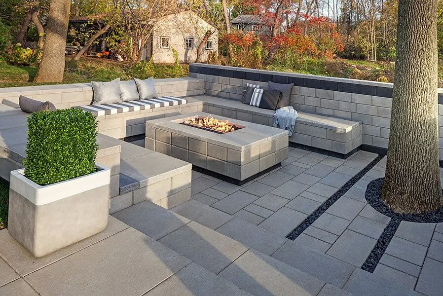 Outdoor patio with built-in seating, fire pit, and stone pavers in a backyard setting with a tree.