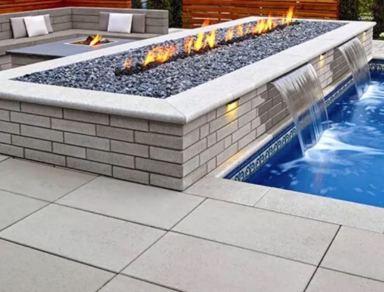 Rectangular pool with cascading waterfalls, fire pit, and stone patio.
