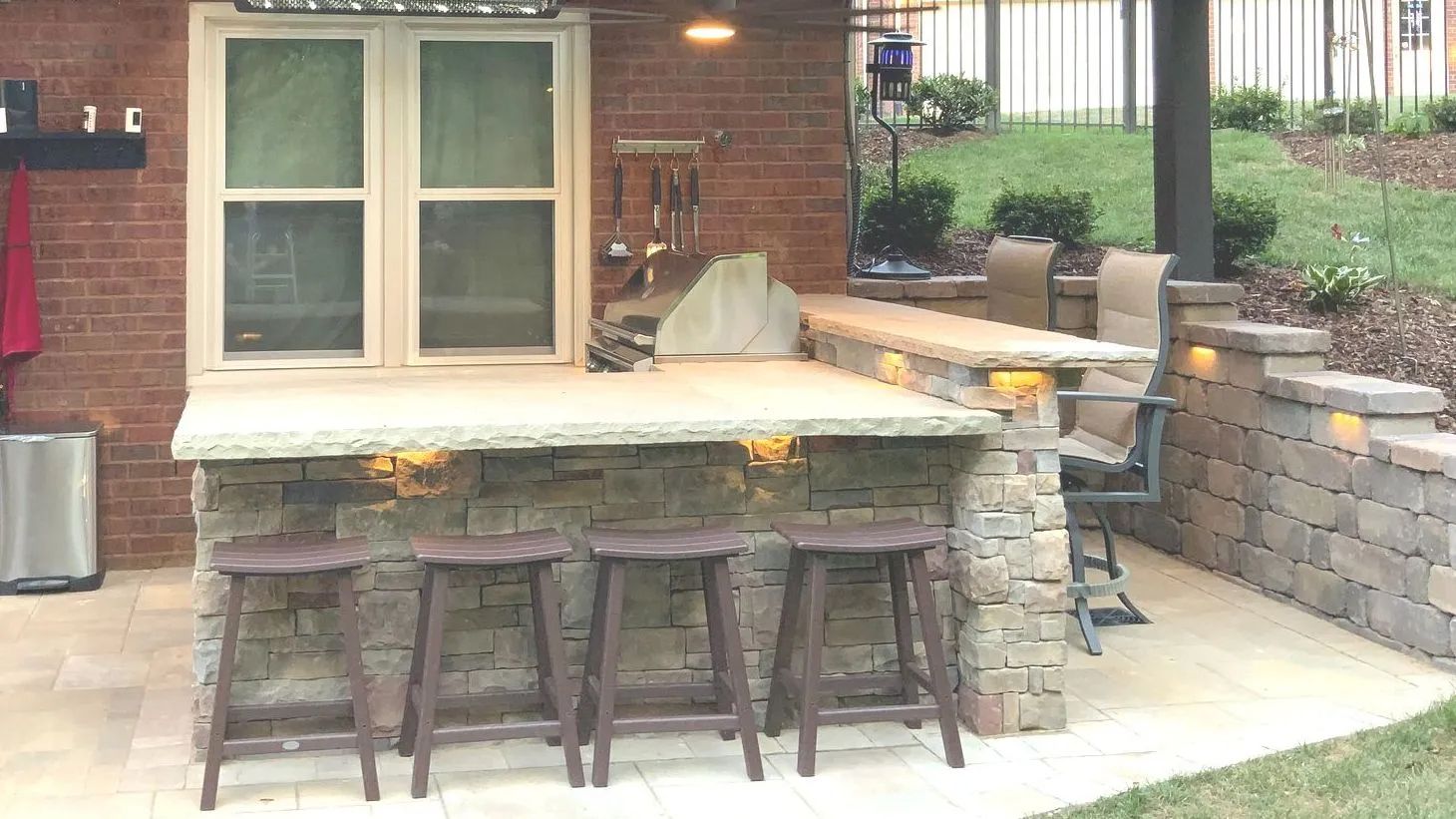 Outdoor bar with stone facade, counter, stools, and built-in grill, patio setting.