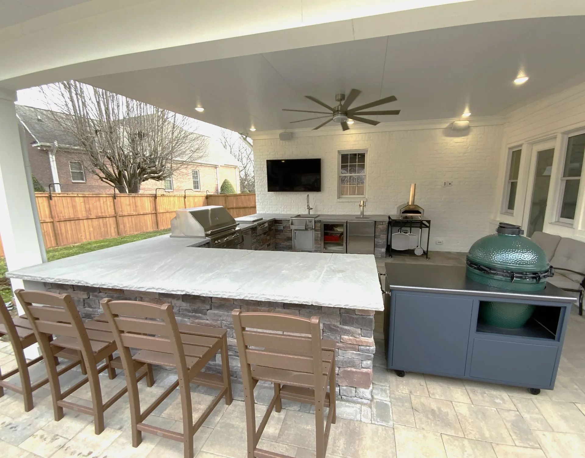 Outdoor kitchen with bar seating, grill, smoker, and TV under a covered patio.