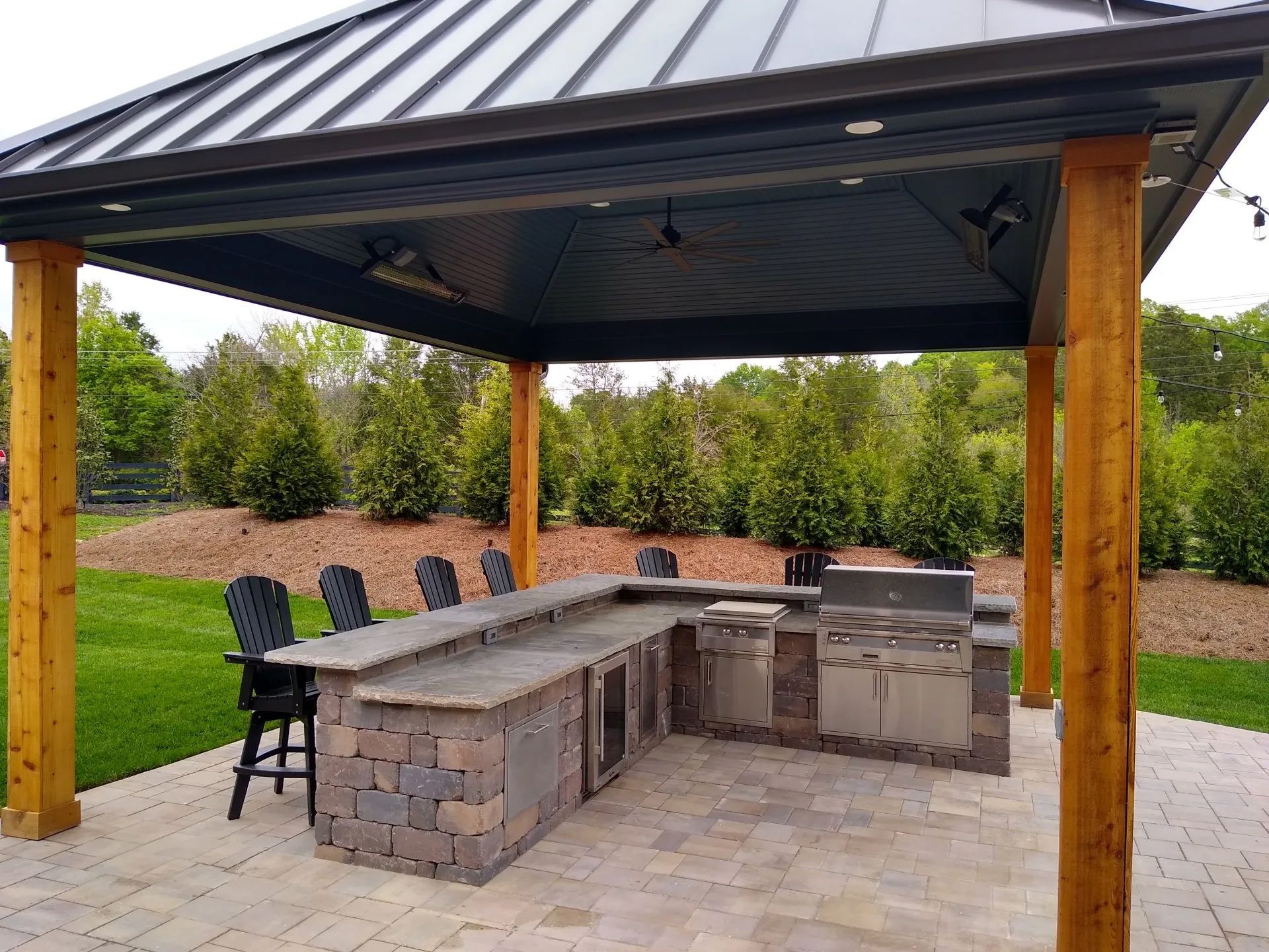 Outdoor kitchen with a gazebo, bar seating, and a built-in grill on a stone patio.