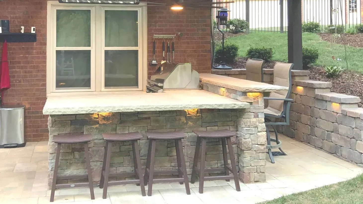 Outdoor stone bar with stools and window, brick wall, and tiered seating area.