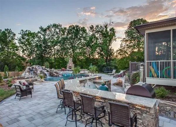 Outdoor patio with bar, pool, waterfall, and trees at dusk.
