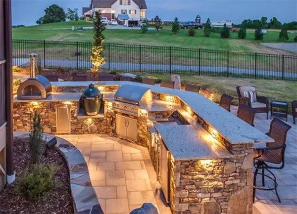 Outdoor kitchen with pizza oven, grill, stone counter, and patio seating.