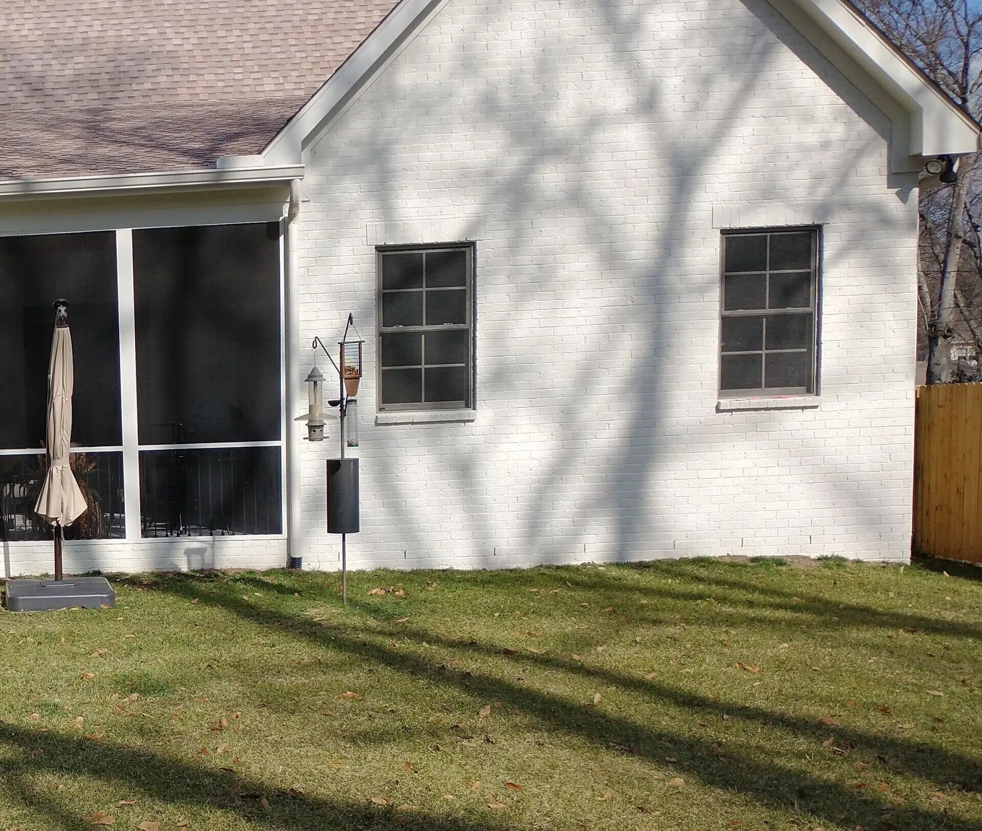 White brick house exterior with two windows and a screened porch, casting tree shadows.