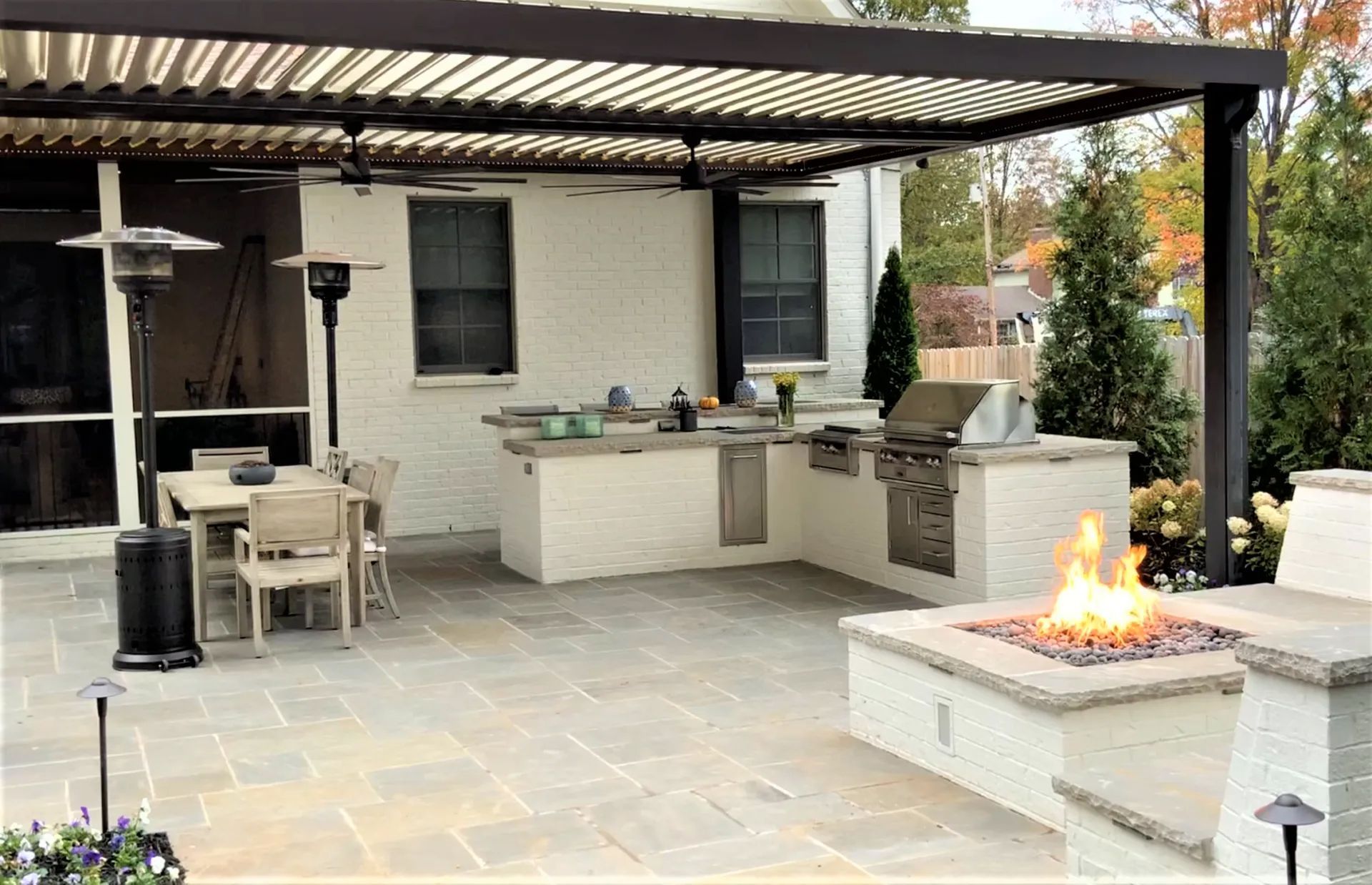 Outdoor kitchen with a pergola, fireplace, and dining area on a stone patio.