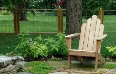 Wooden Adirondack chair on a stone patio, greenery and fence in the background.
