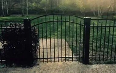 Black metal gate in front of a green yard and trees.