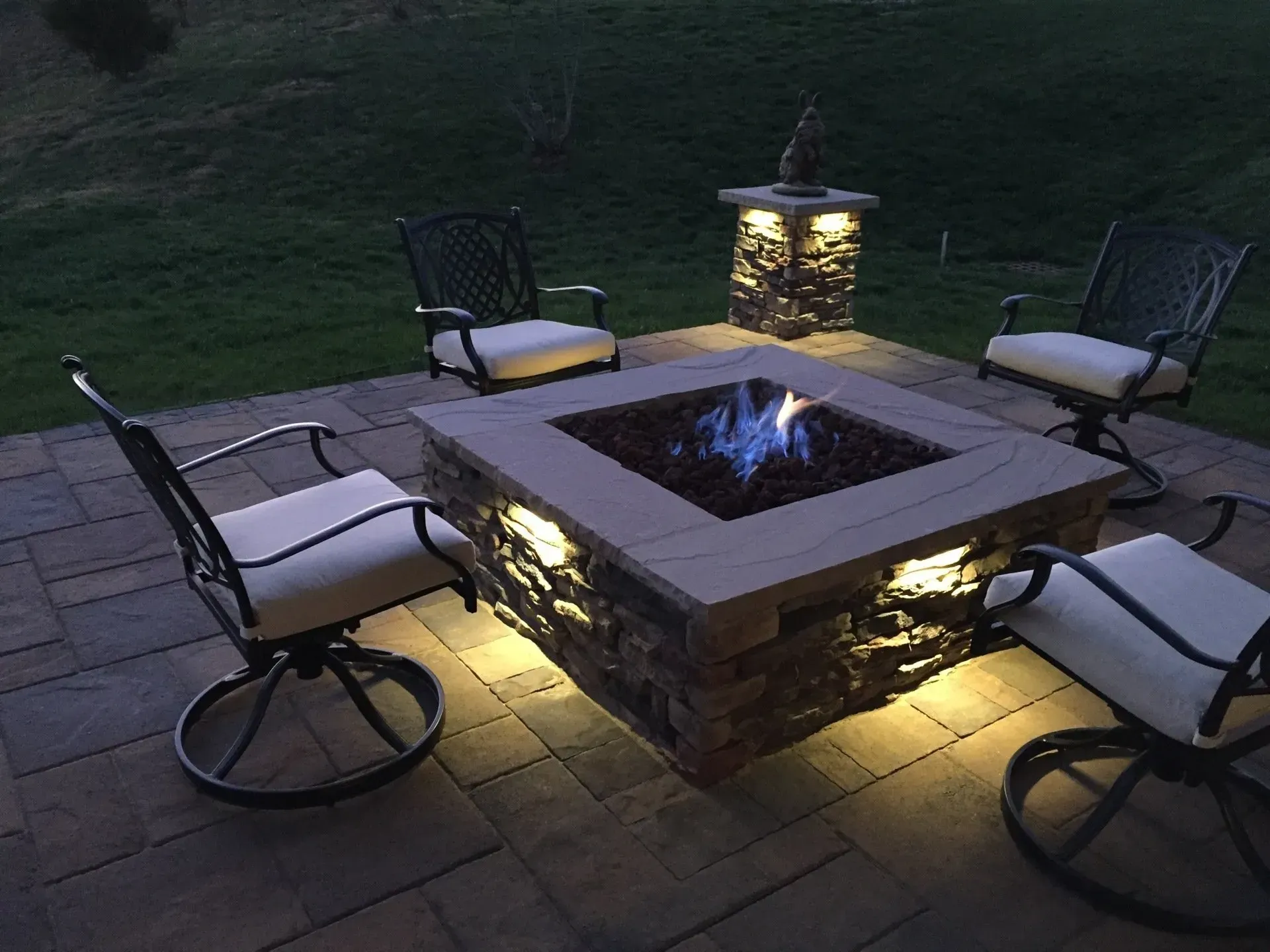 Outdoor seating area with lit fire pit and stone accents at dusk.
