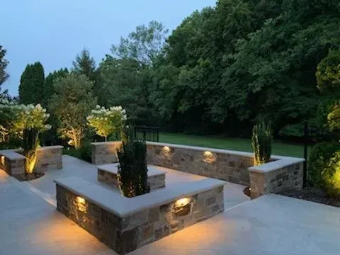Outdoor patio with stone planters, illuminated by warm lights, surrounded by greenery.