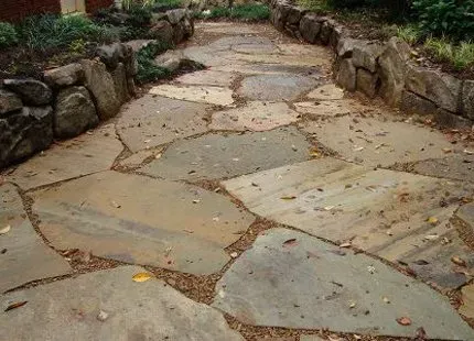 Stone path with rock borders, leading through a garden, covered with leaves.