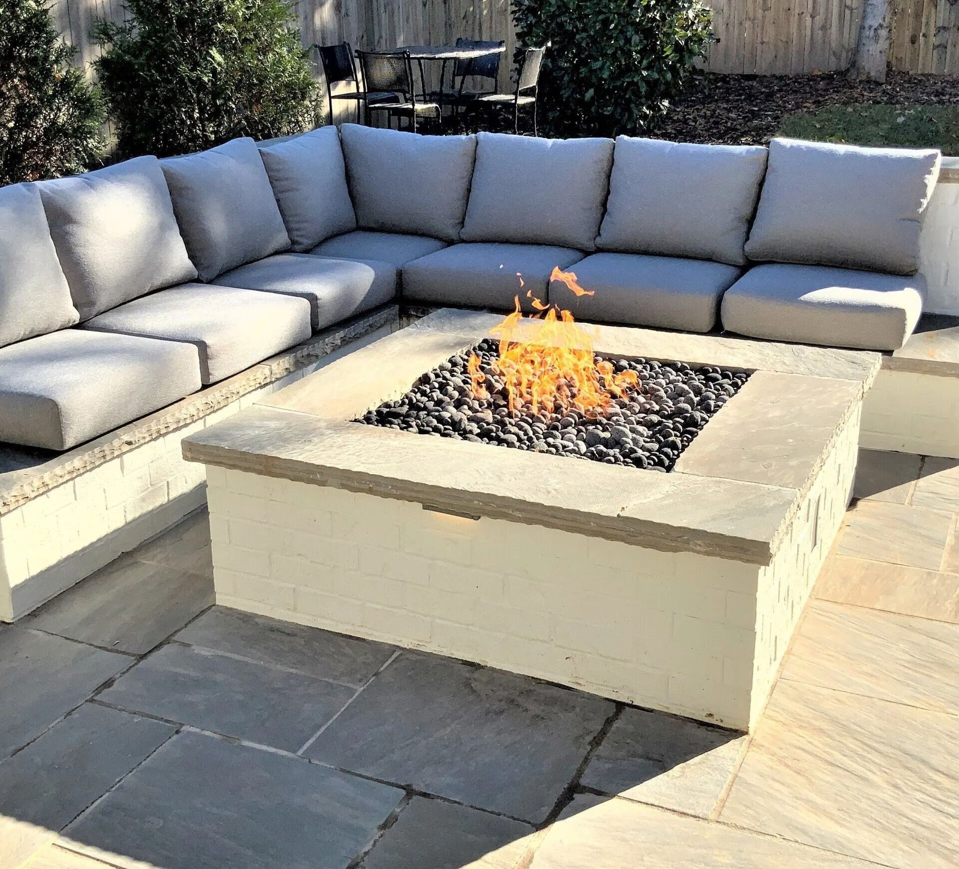 Outdoor sectional sofa around a lit fire pit on a stone patio.