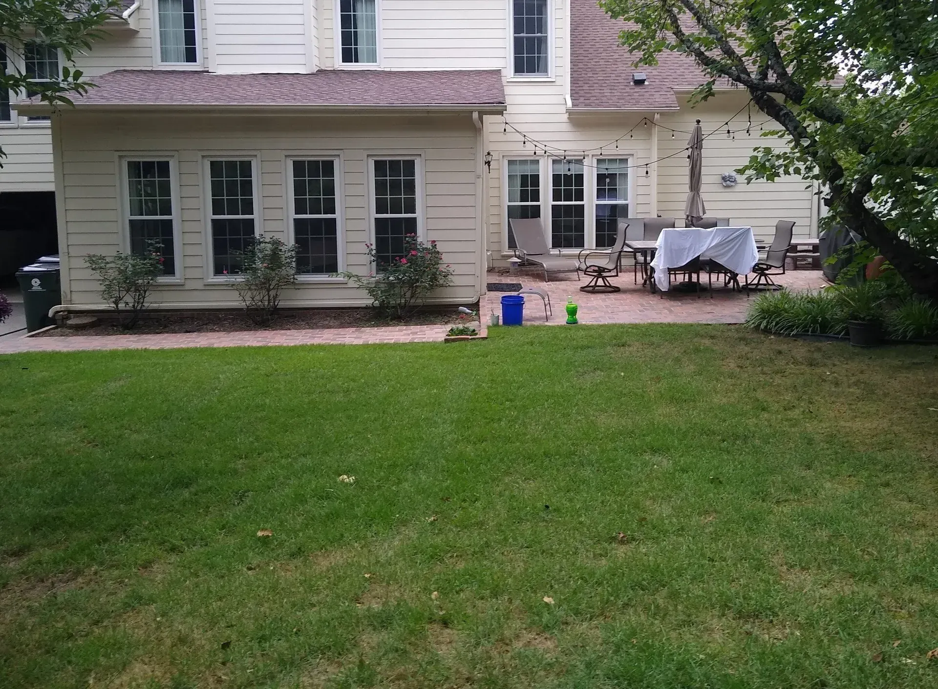 Backyard view of a house with a patio and grass lawn. Beige siding, white windows, and a table set.