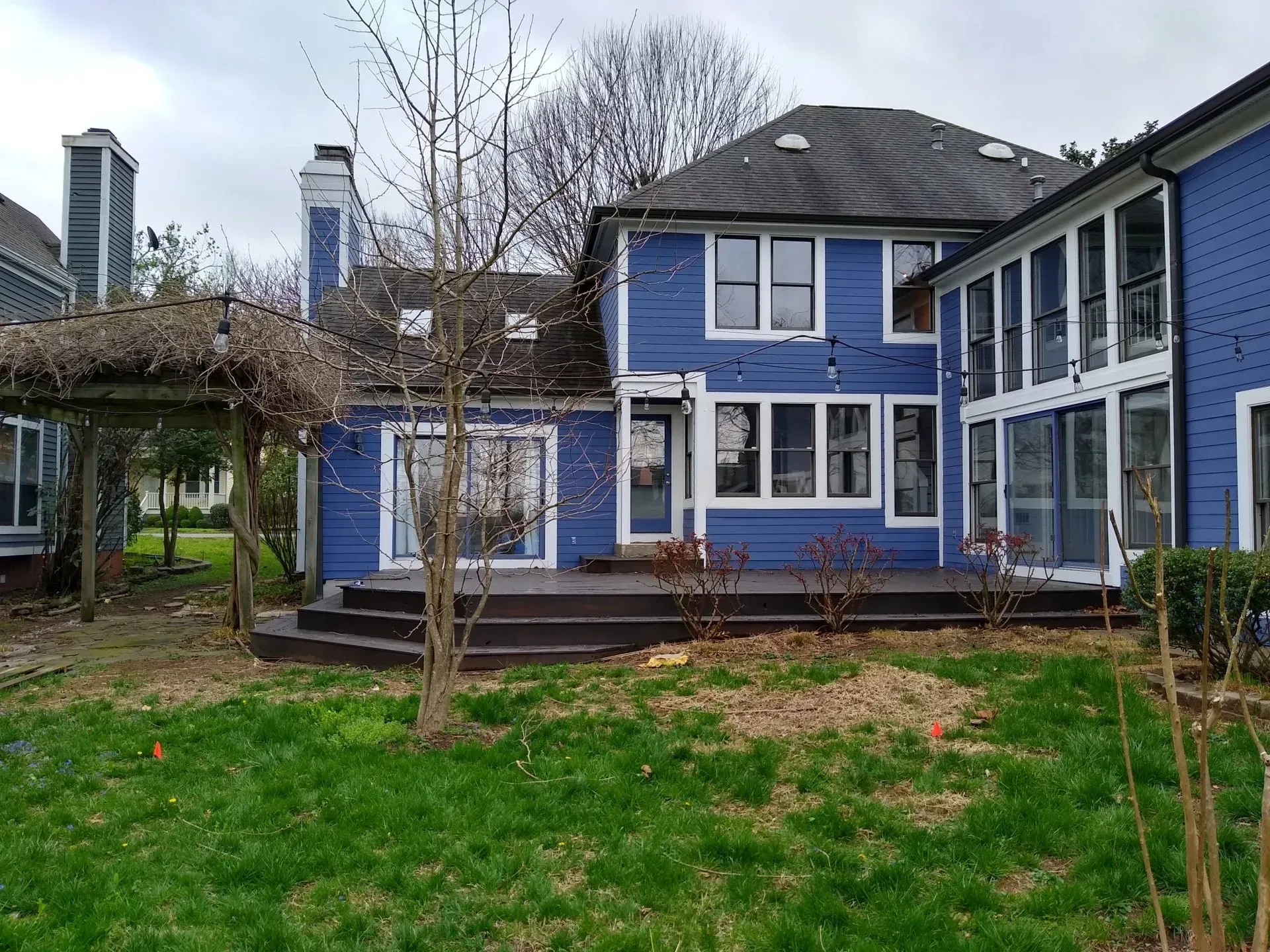 Blue house with a deck and pergola, set on green grass. Overcast day.