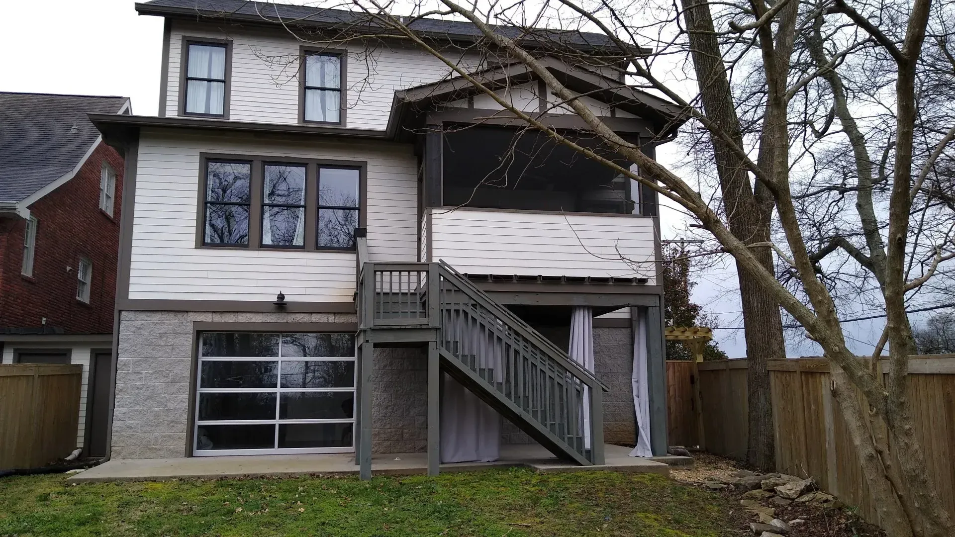 Two-story house with a screened porch and stairs to a lower level. Garage door is visible.
