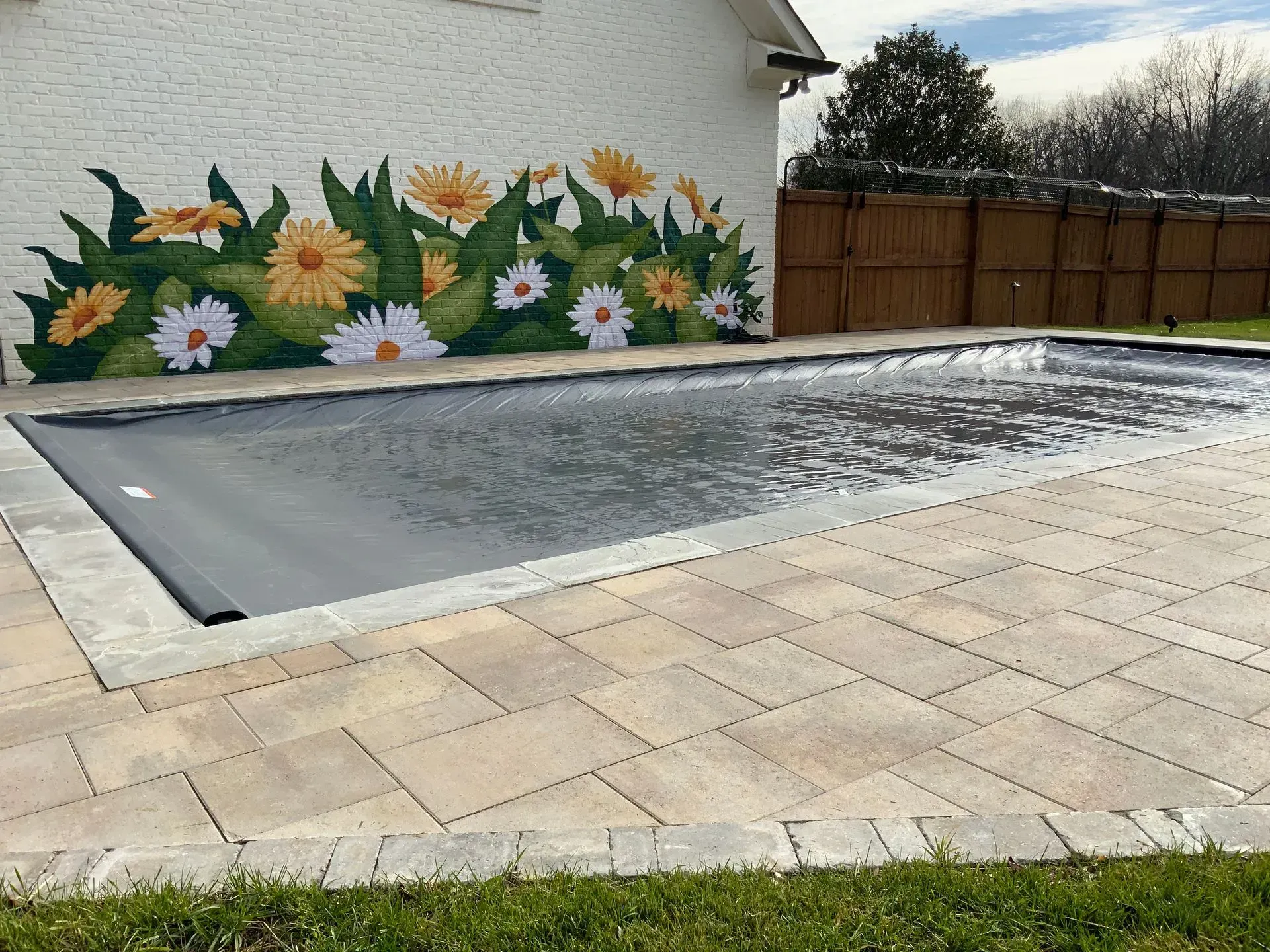 Pool with cover and surrounding patio. Floral mural on white wall.