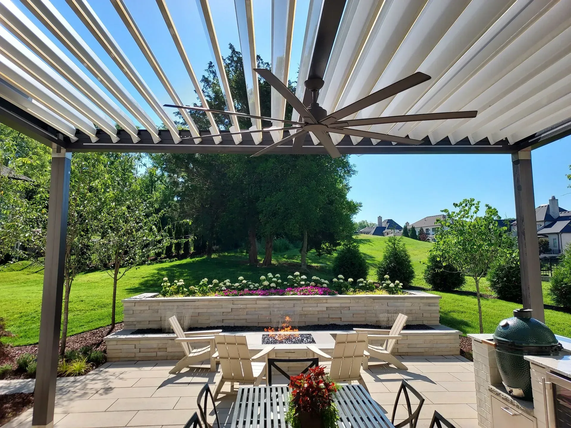 Outdoor patio with adjustable pergola roof, fan, fireplace, seating, and garden view.