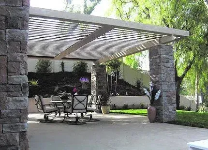 Patio with stone columns supporting a slatted pergola, table, chairs, and potted plants.