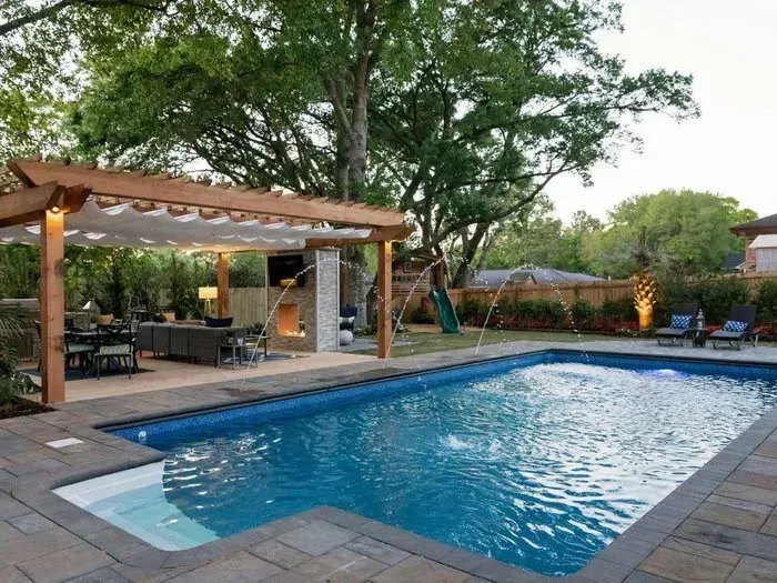 Backyard pool with pergola, outdoor kitchen, and landscaping.