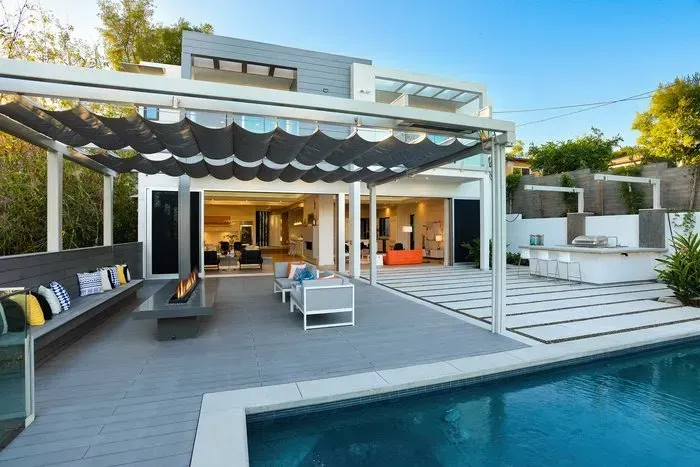 Modern home with pool, patio, and retractable shade structure; gray and white exterior.