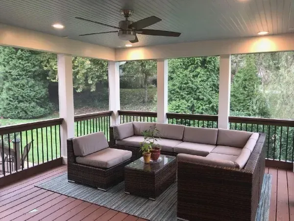 Screened-in porch with brown wicker furniture, ceiling fan, and view of a green backyard.