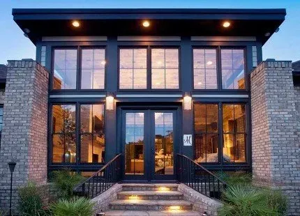 Modern home exterior with large glass windows and brick accents; front entrance with steps and double doors.