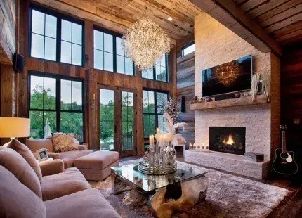Living room with large windows, fireplace, crystal chandelier, and a brown sofa.