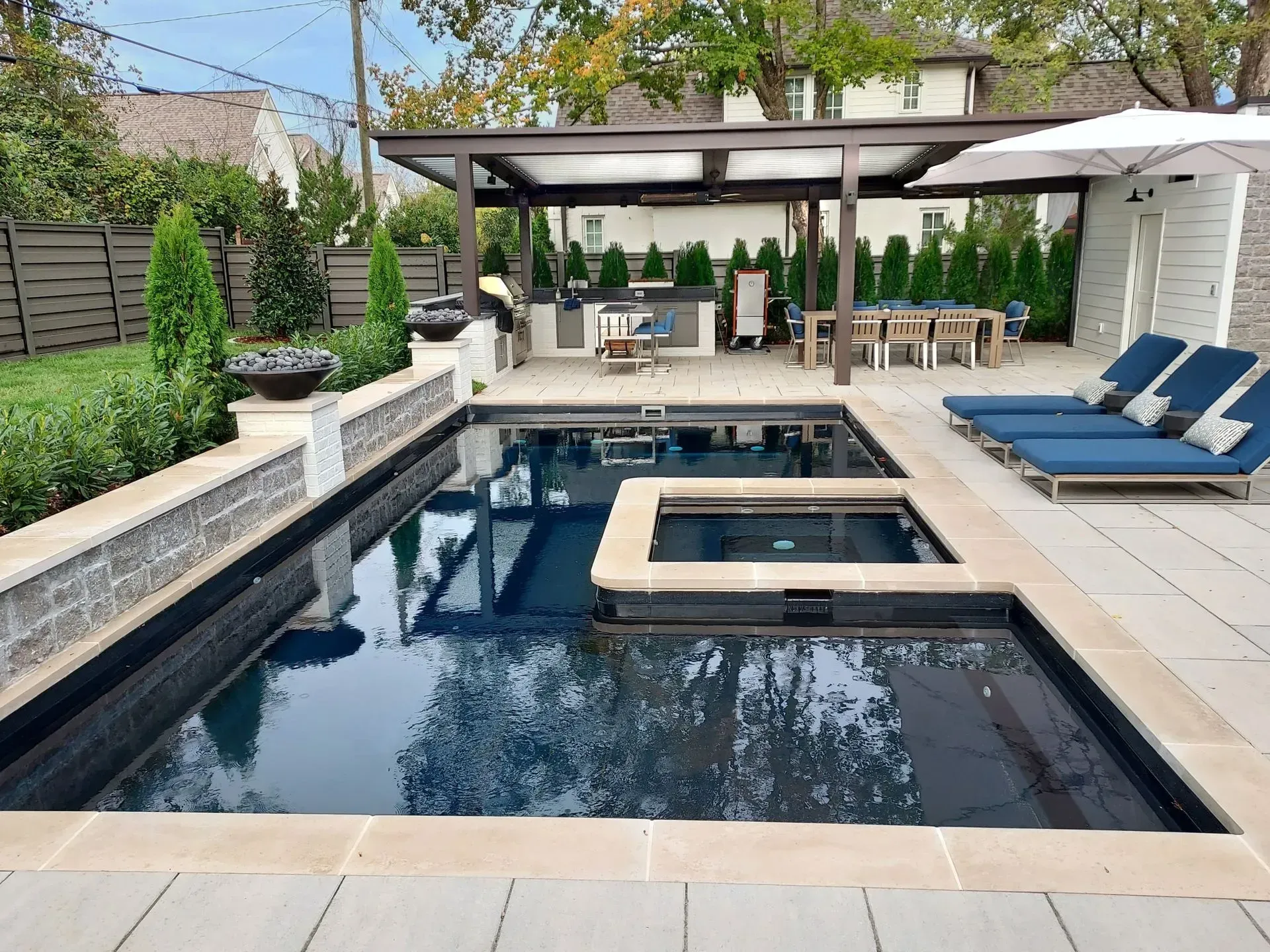 Backyard pool area with a dark blue pool, jacuzzi, outdoor kitchen, and dining area.