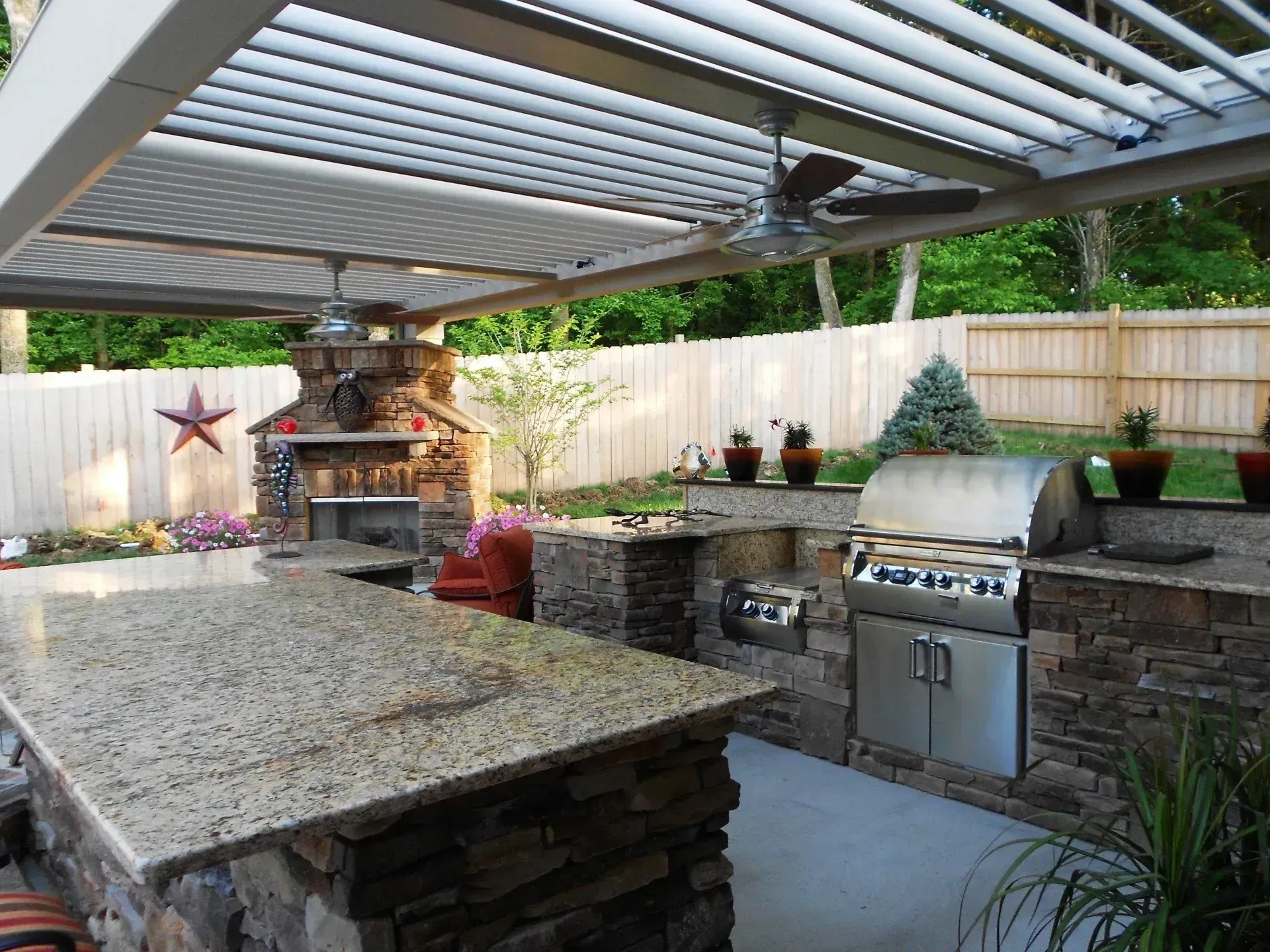 Outdoor kitchen with stone counters, grill, fireplace, and pergola roof.