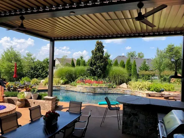 Outdoor patio with a pool view, featuring a dining area, a bar, and ceiling fans.