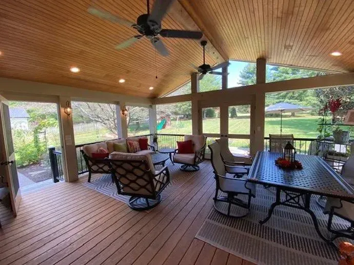 Covered outdoor patio with seating and ceiling fans; glass windows overlook a backyard.