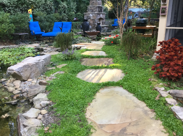 Garden path with stone pavers, blue chairs, and a stone fountain amid greenery