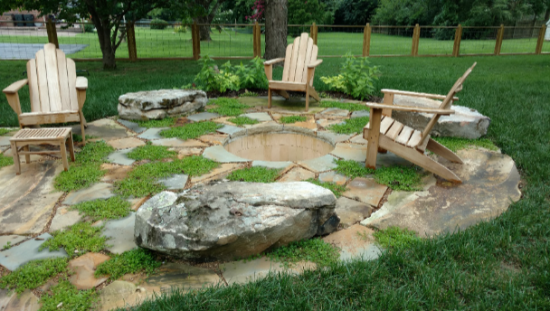 Stone fire pit with four wooden chairs in a grassy park area