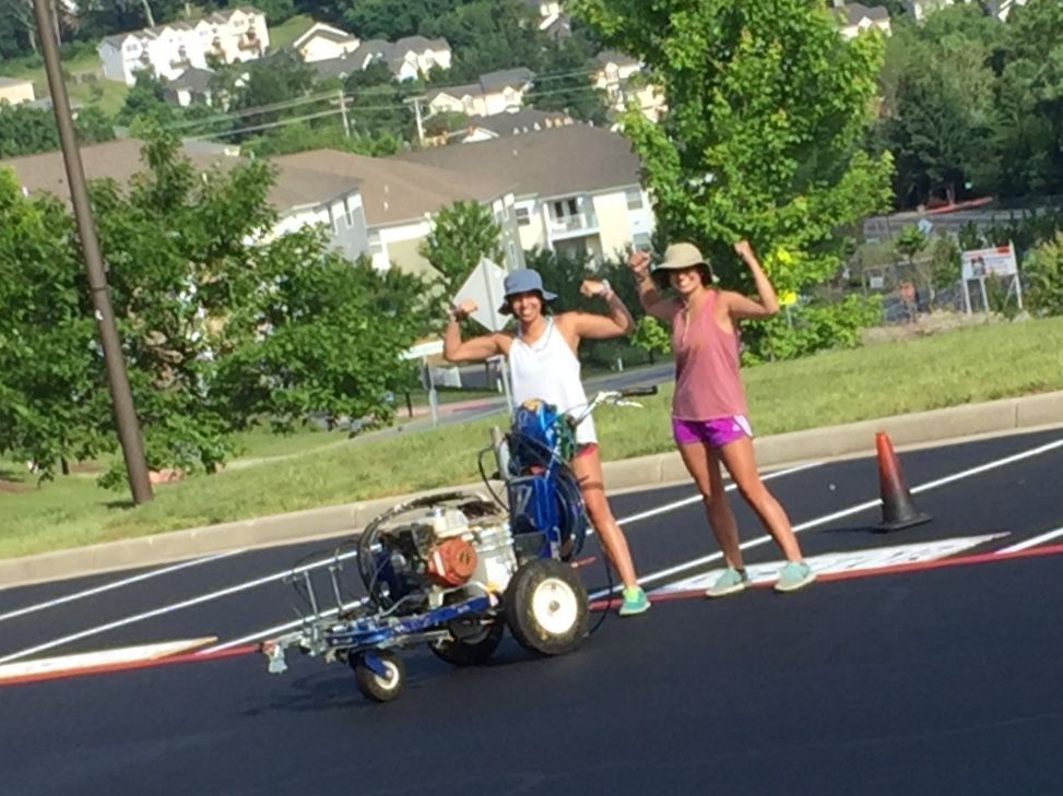 two people are standing next to a machine that is painting a road