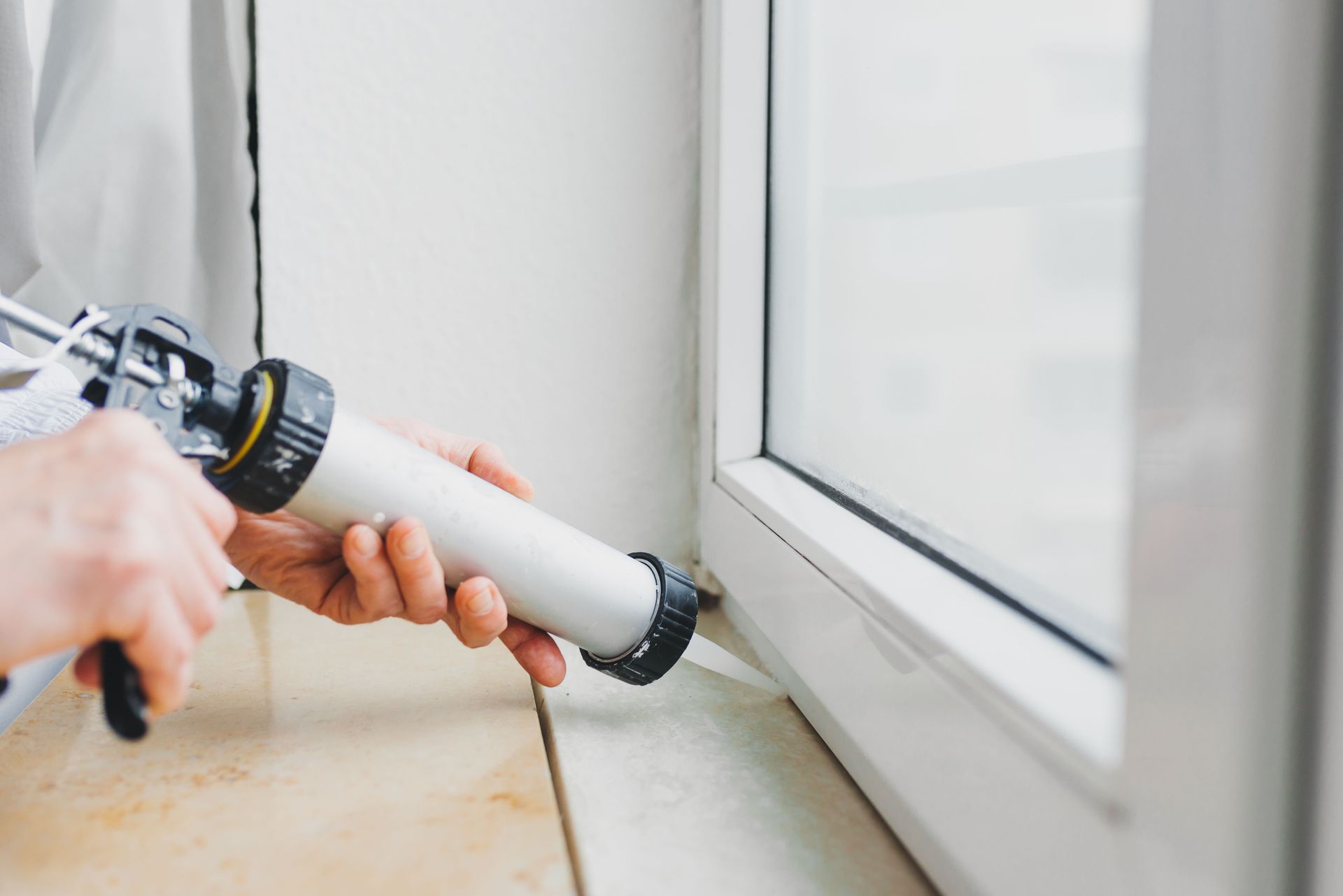 Person using a caulking gun to seal around a window frame.
