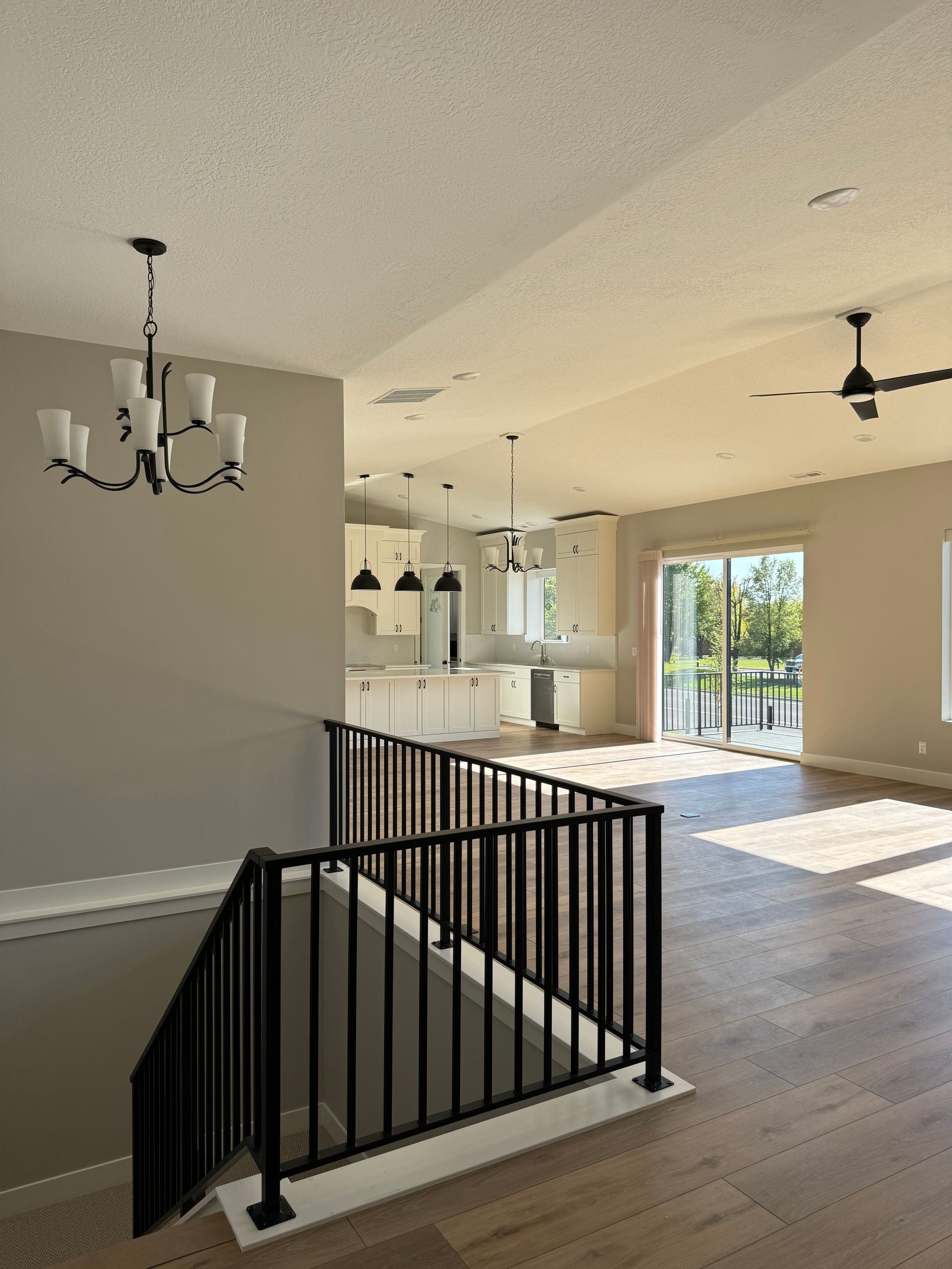 An empty house with a black railing and a chandelier hanging from the ceiling.