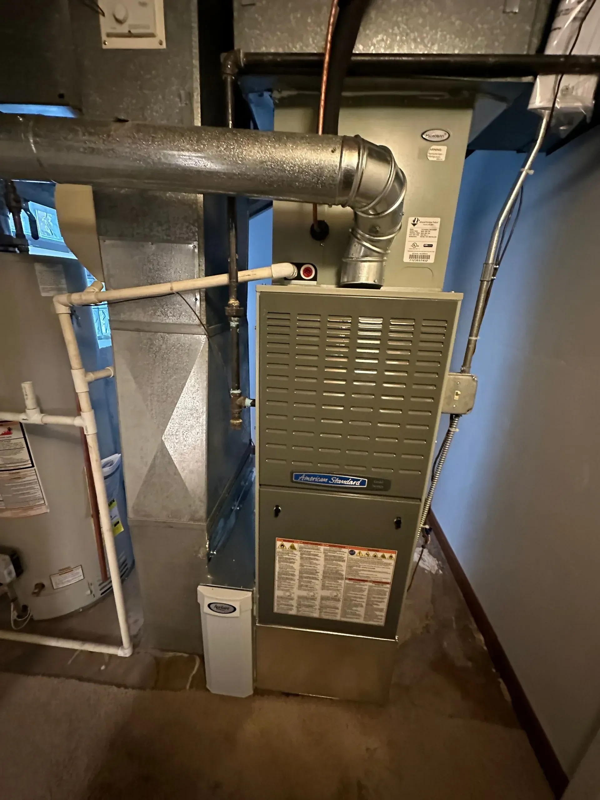Furnace and water heater in a basement, with ductwork and pipes.