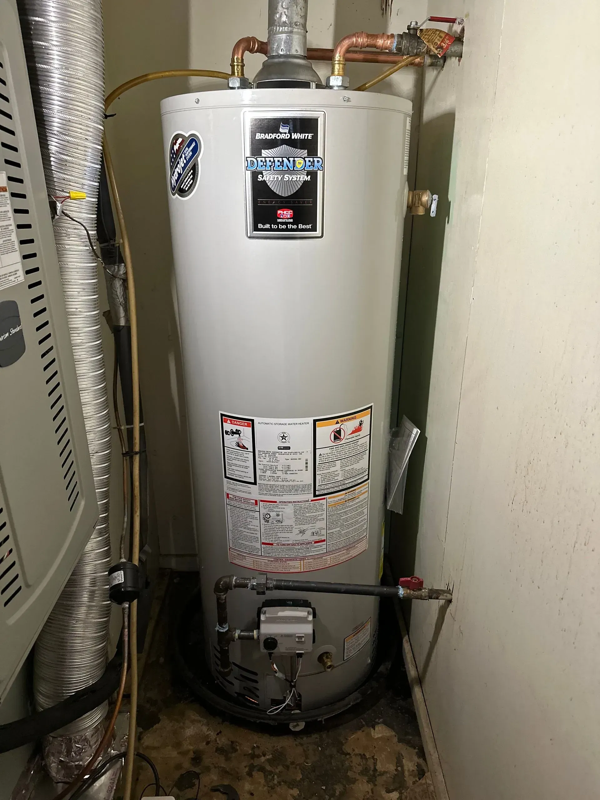 Water heater in a small utility closet, with pipes and venting.
