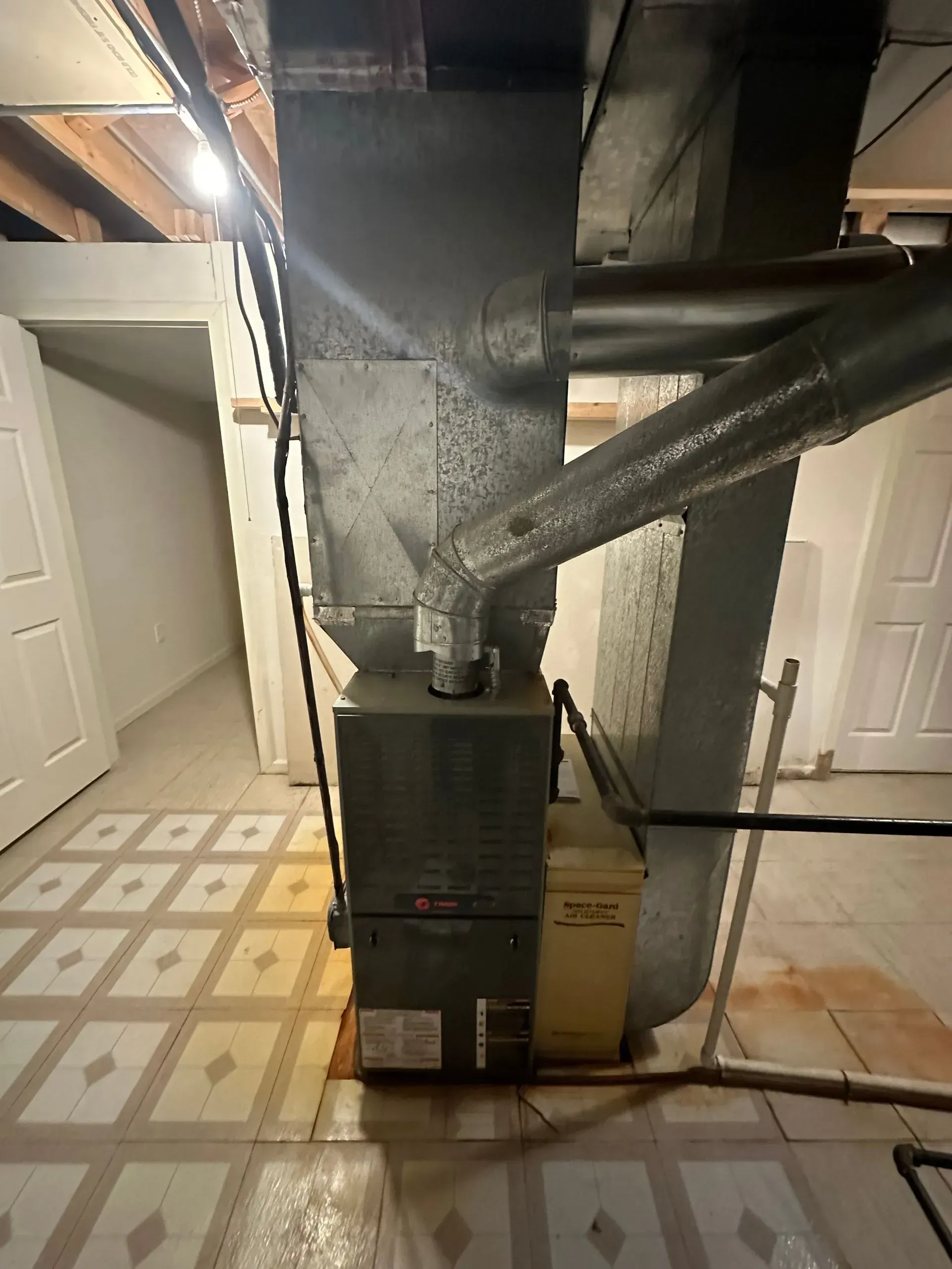 Furnace and ductwork in a basement with white doors and tiled floor.