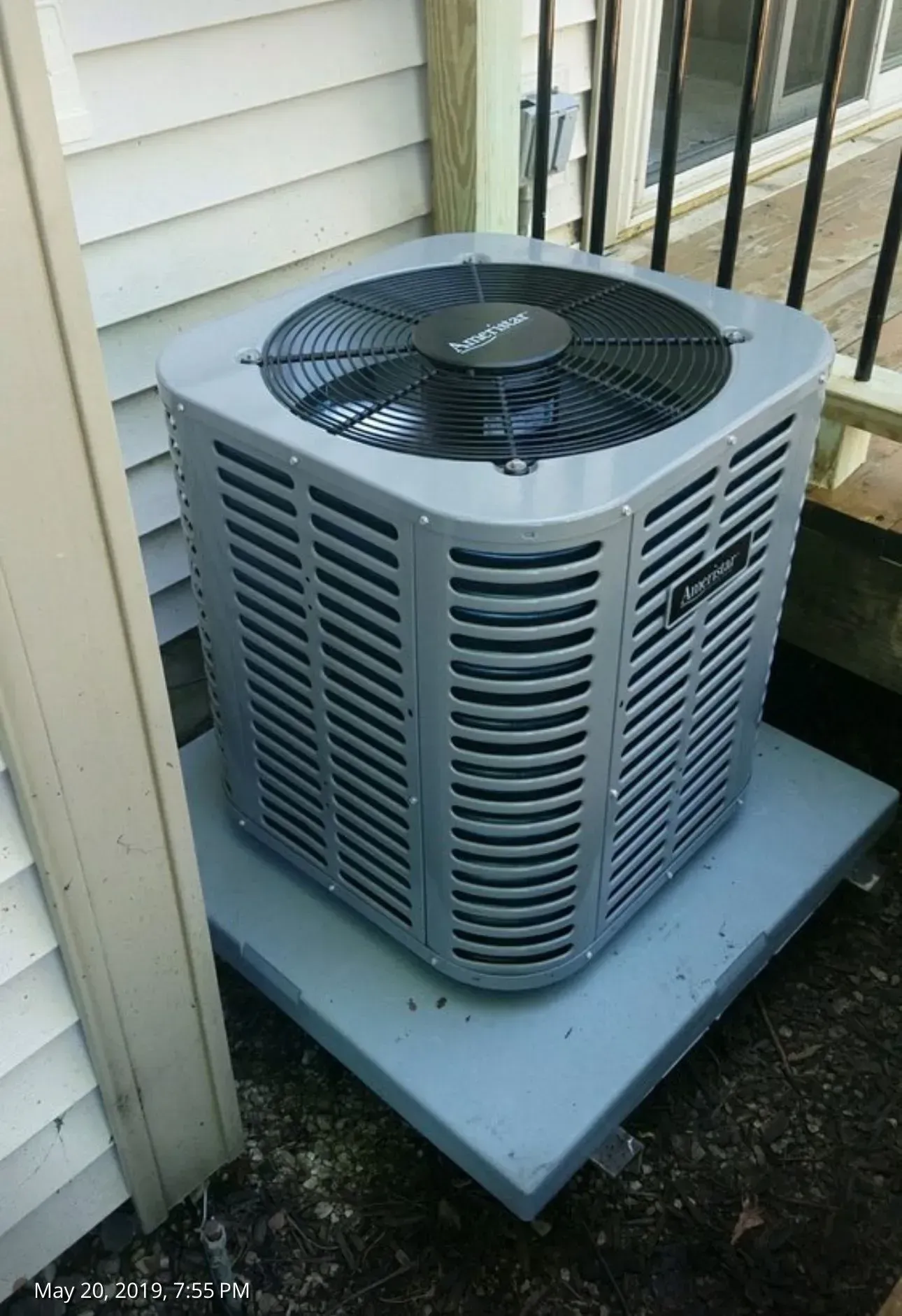 An air conditioning unit in a gray metal enclosure on a gray platform next to a white wall.
