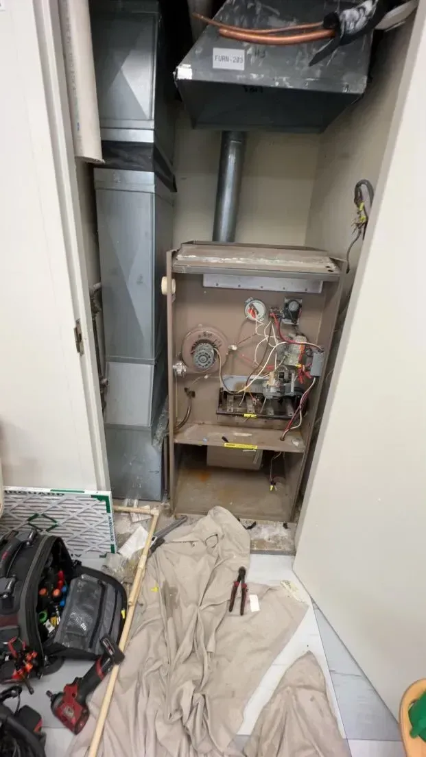 Furnace in a closet, partially disassembled. Tools and drop cloth on floor.
