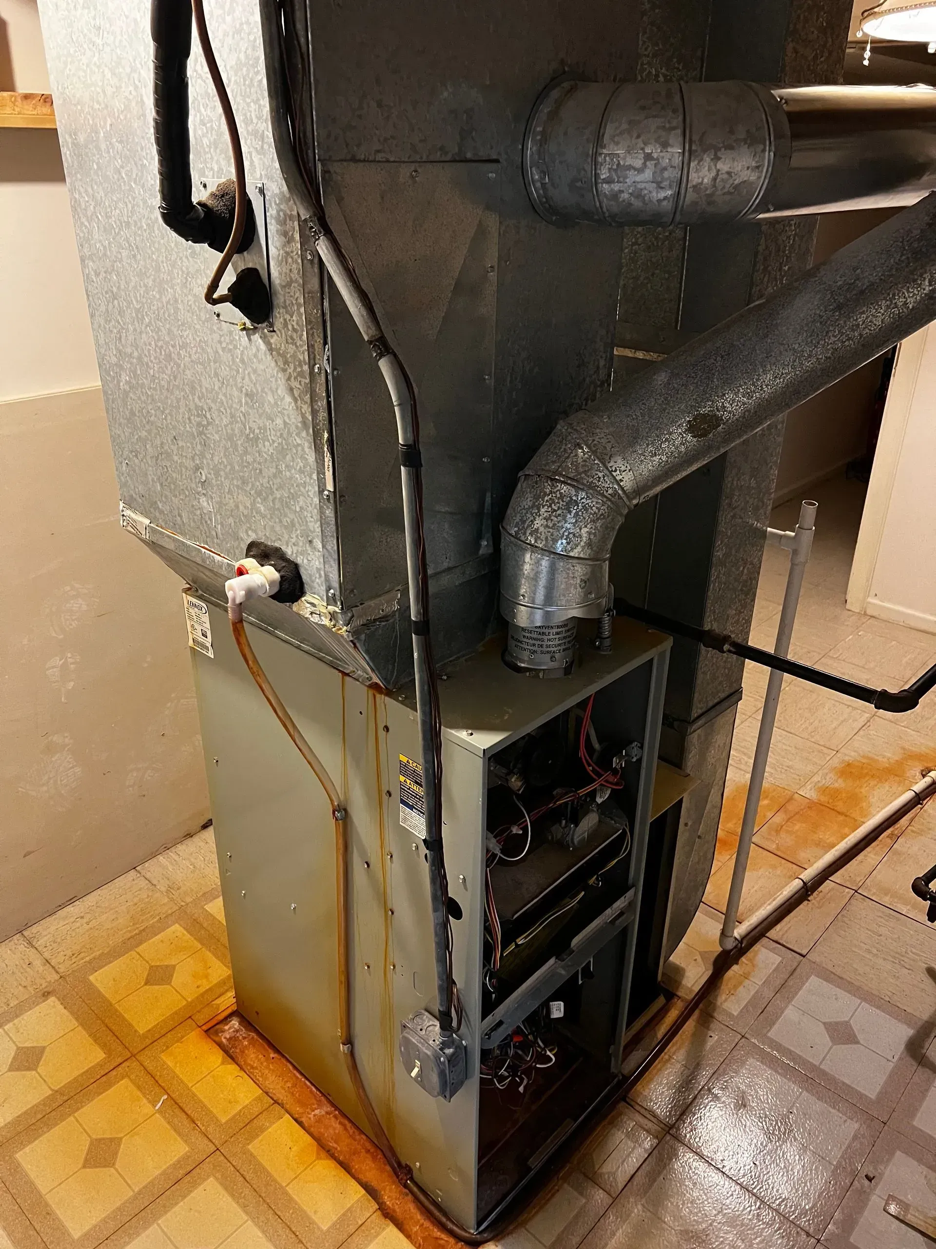 A furnace is leaking water. The metal unit sits on a tile floor with water around it.