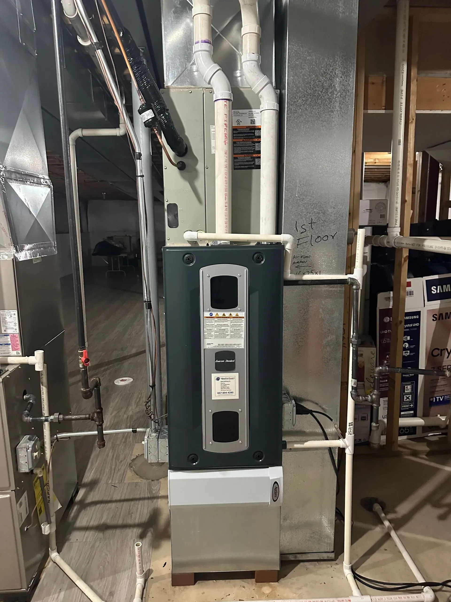 Furnace unit in a basement, with ductwork, pipes, and wiring visible.