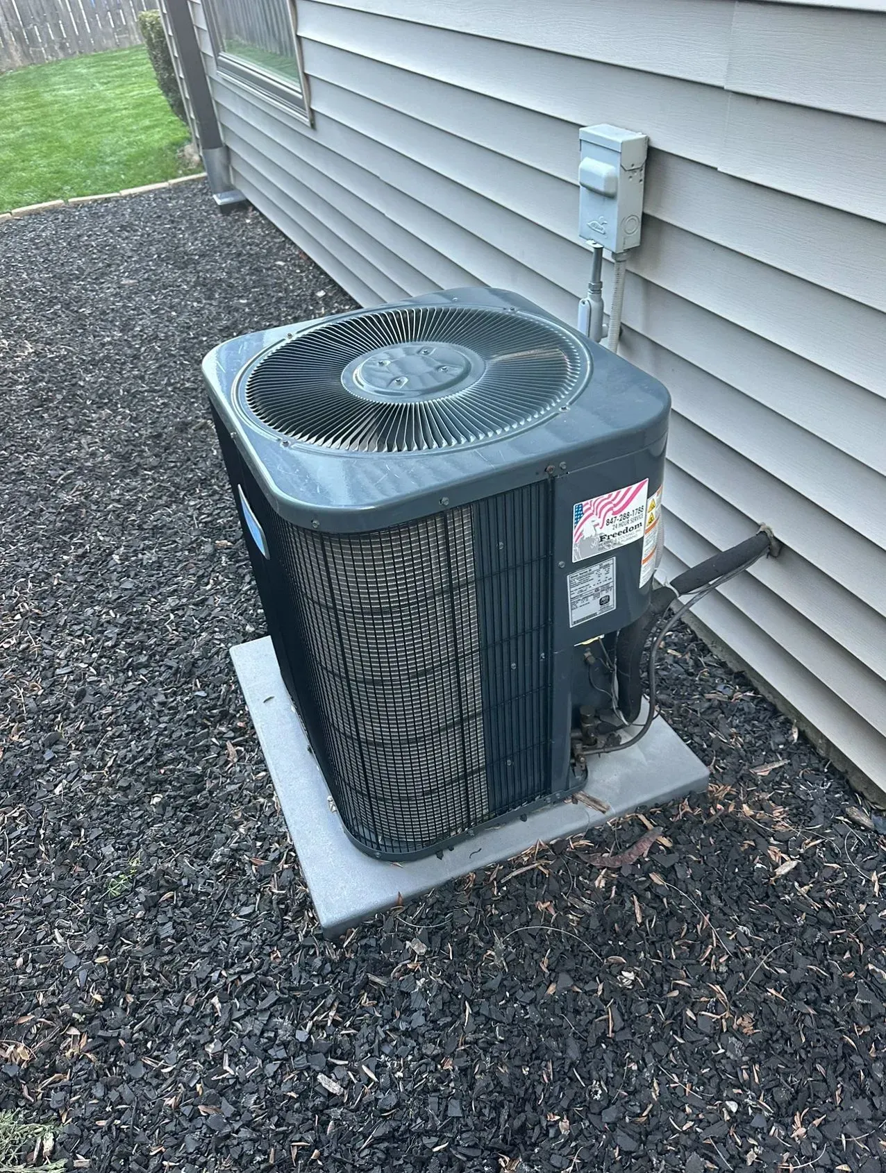 Air conditioning unit outside a building on a concrete pad, surrounded by dark mulch.