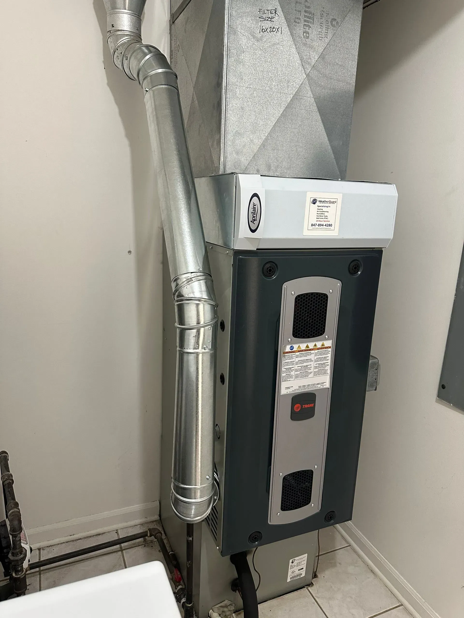 A furnace and ductwork in a laundry room, with gray and silver metal against a white wall.