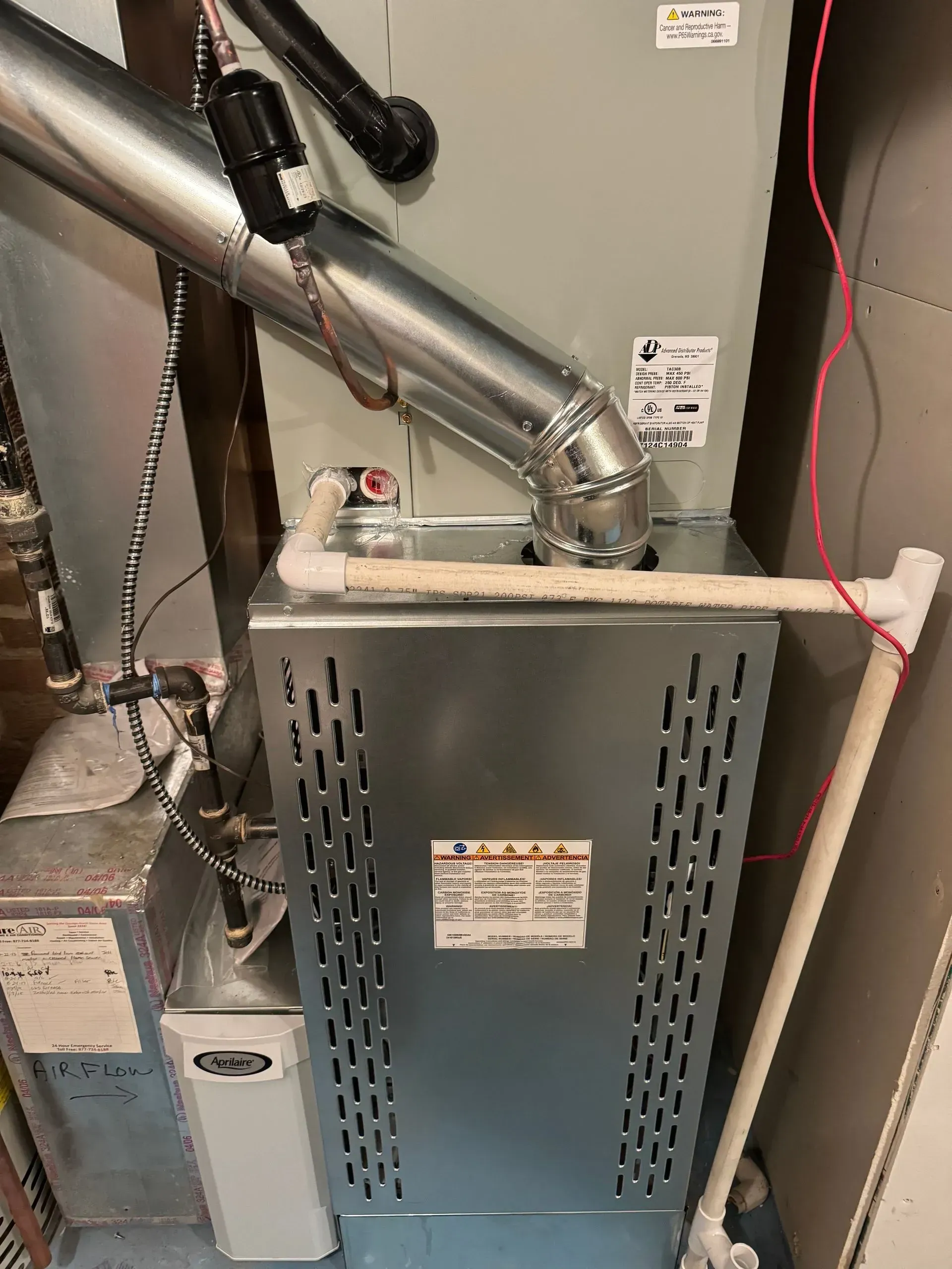 A silver furnace with vents and pipes in a utility room.